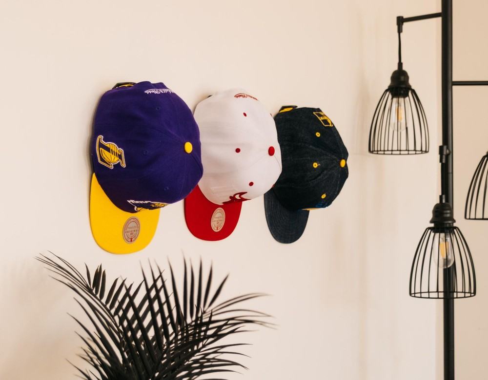 Baseball caps displayed face-forward on Modern JP baseball cap display hooks beside a floor lamp